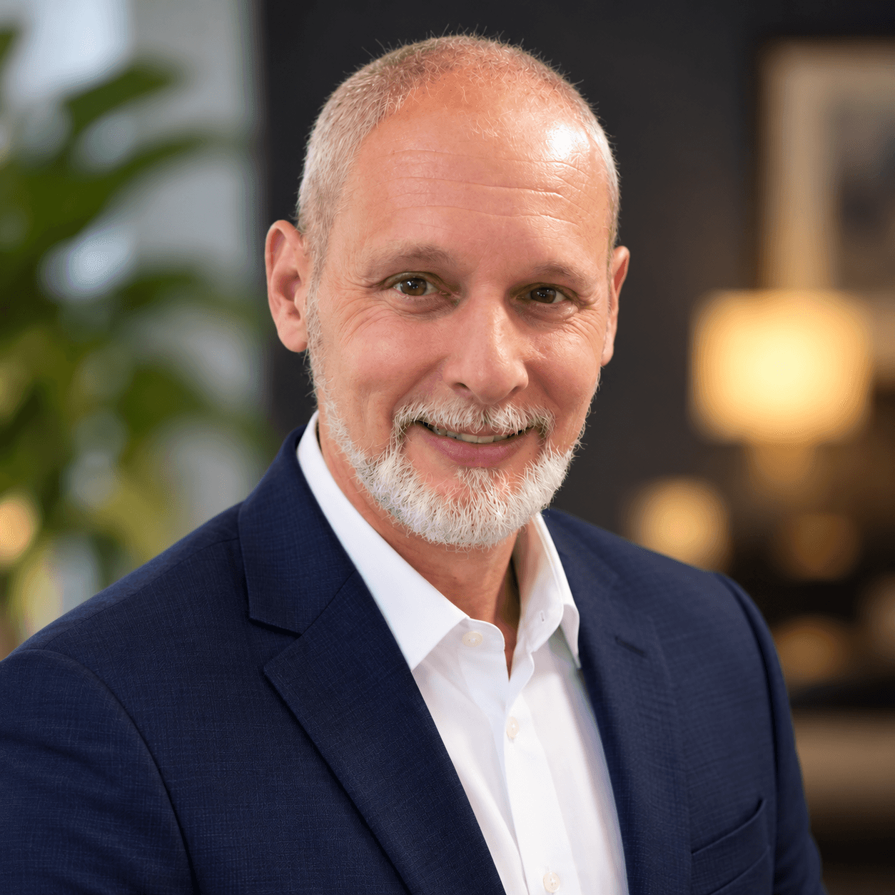 Smiling middle-aged man with gray hair and beard, wearing a navy blazer and white shirt.
